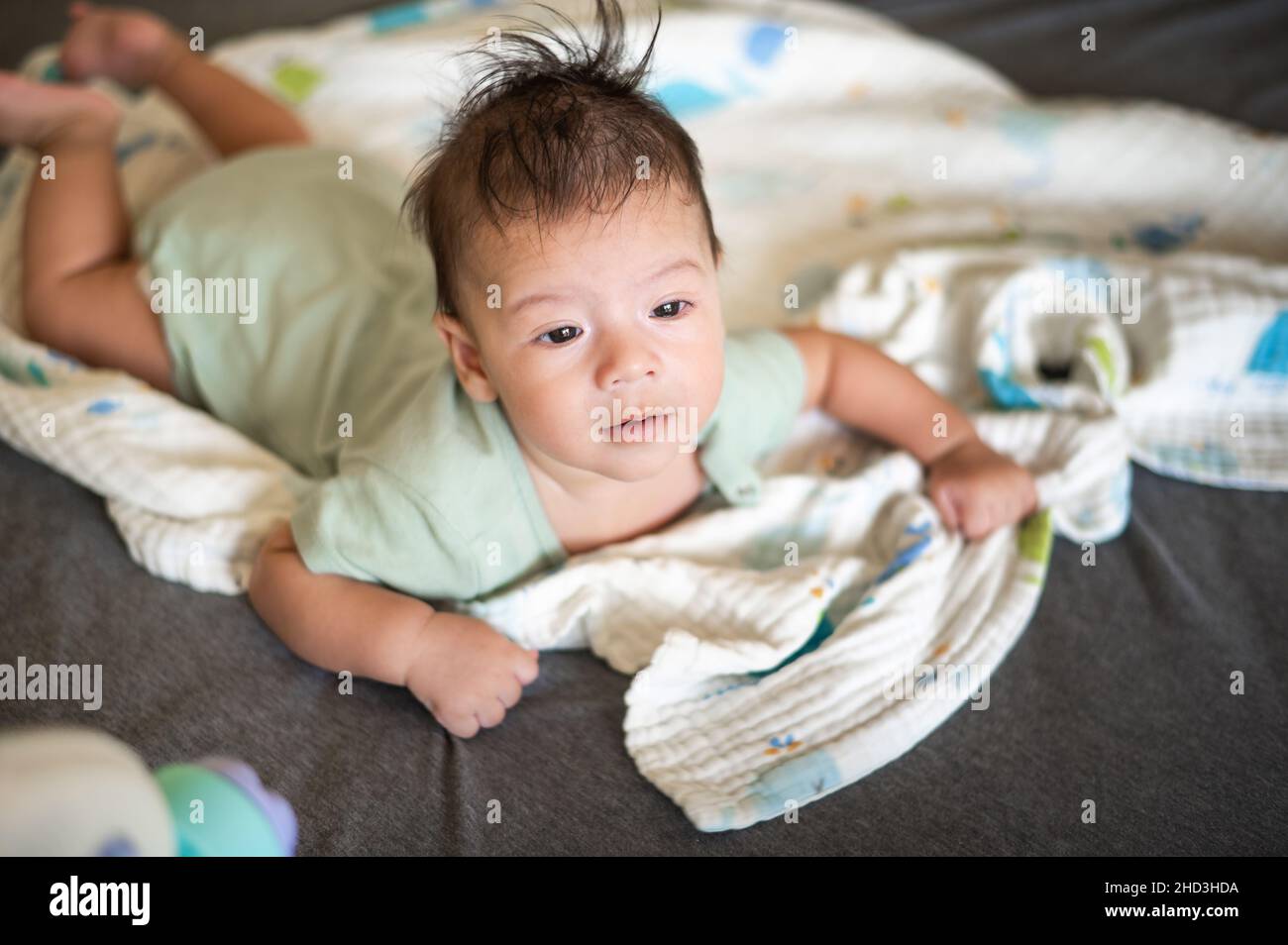 Adorable 2 months old mixed race newborn baby boy lying on his tummy on the bed lifting head and playing Stock Photo