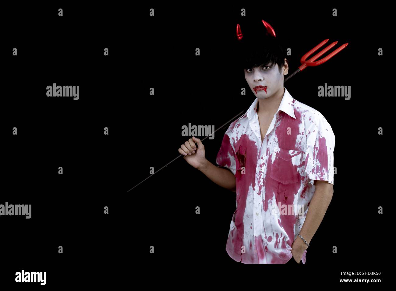 Young Asian man costume in hell, evil on black background with concept for Halloween fashion festival in studio. Teen Asian man in cosplay Halloween. Stock Photo