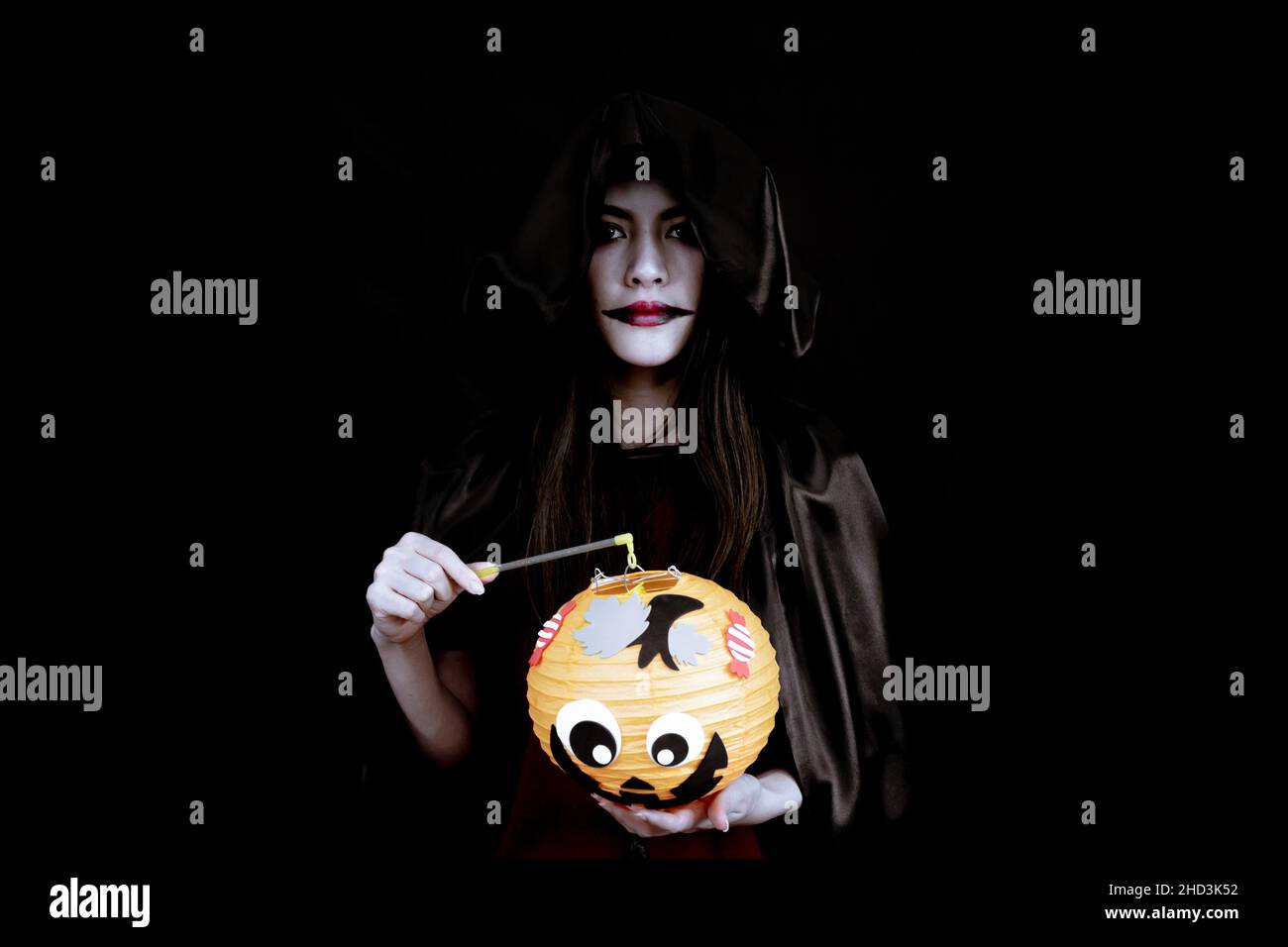 Young Asian woman costume in black witch with hand holding an orange Halloween pumpkin on black background with concept for Halloween fashion festival Stock Photo
