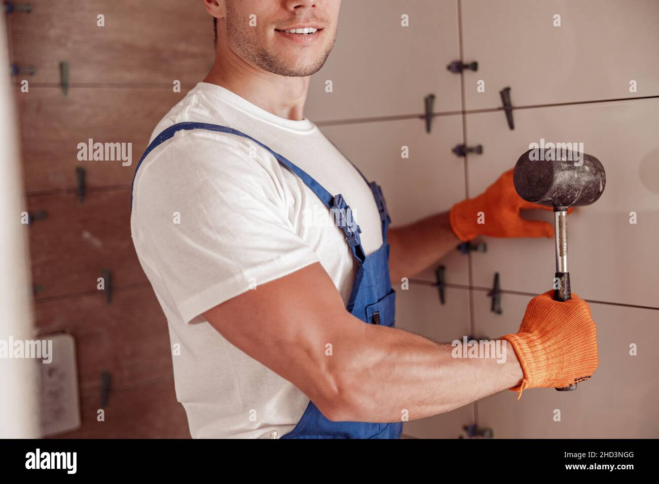 Cheerful male builder installing ceramic wall tile in house Stock Photo