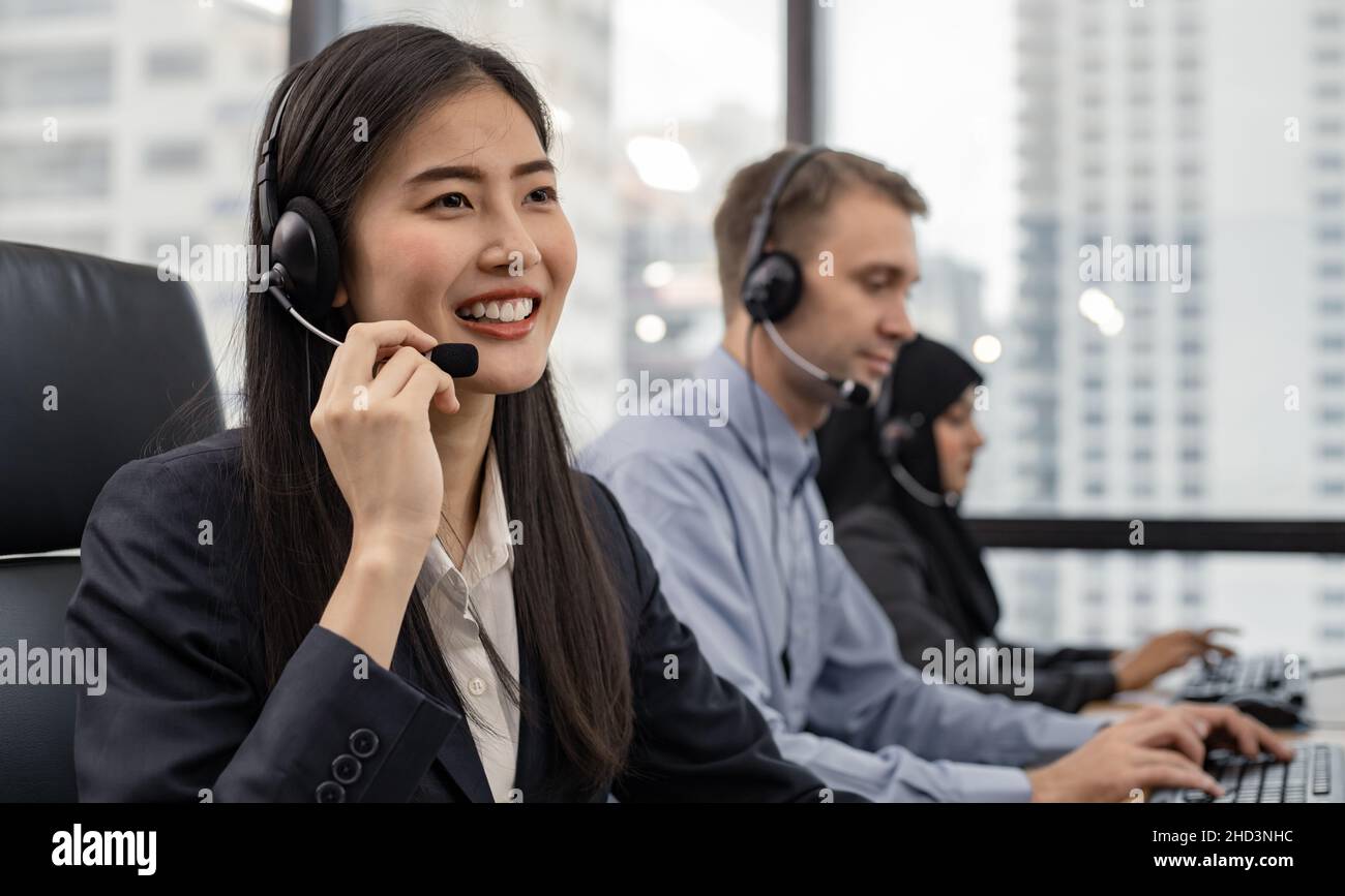 Beautiful Asian woman and group of diverse telemarketing customer service staff team in call center. Call center worker accompanied by team. Smiling o Stock Photo