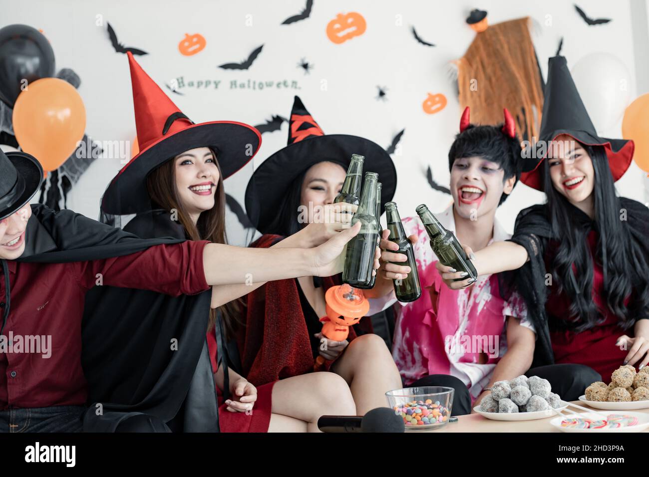 Gang of young Asian in costume witch, wizard with celebrate Halloween party for clink bottle and drink in the room. Group teen Thai with celebrate Hal Stock Photo