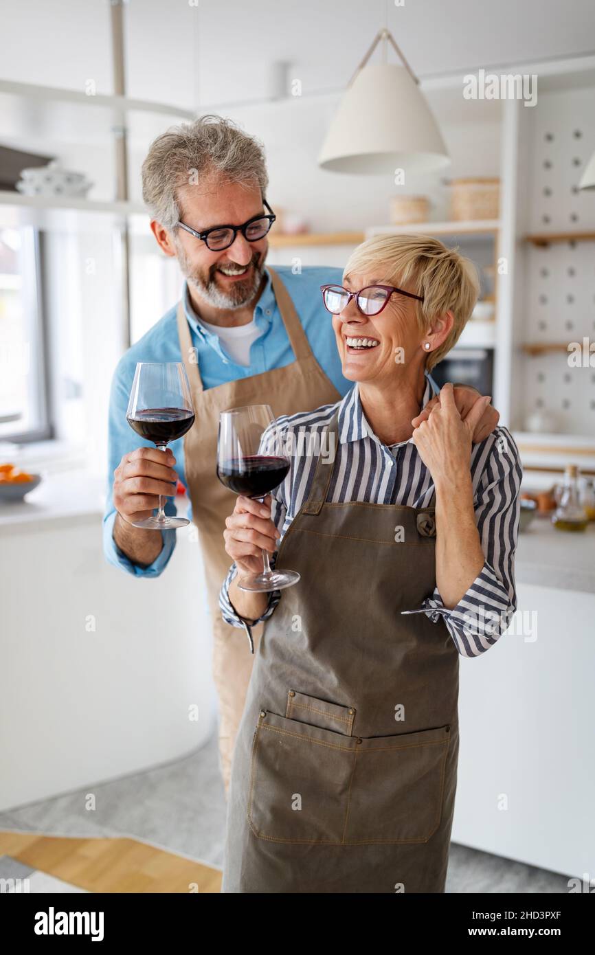 Senior couple having fun, cooking and drinking wine in home kitchen ...