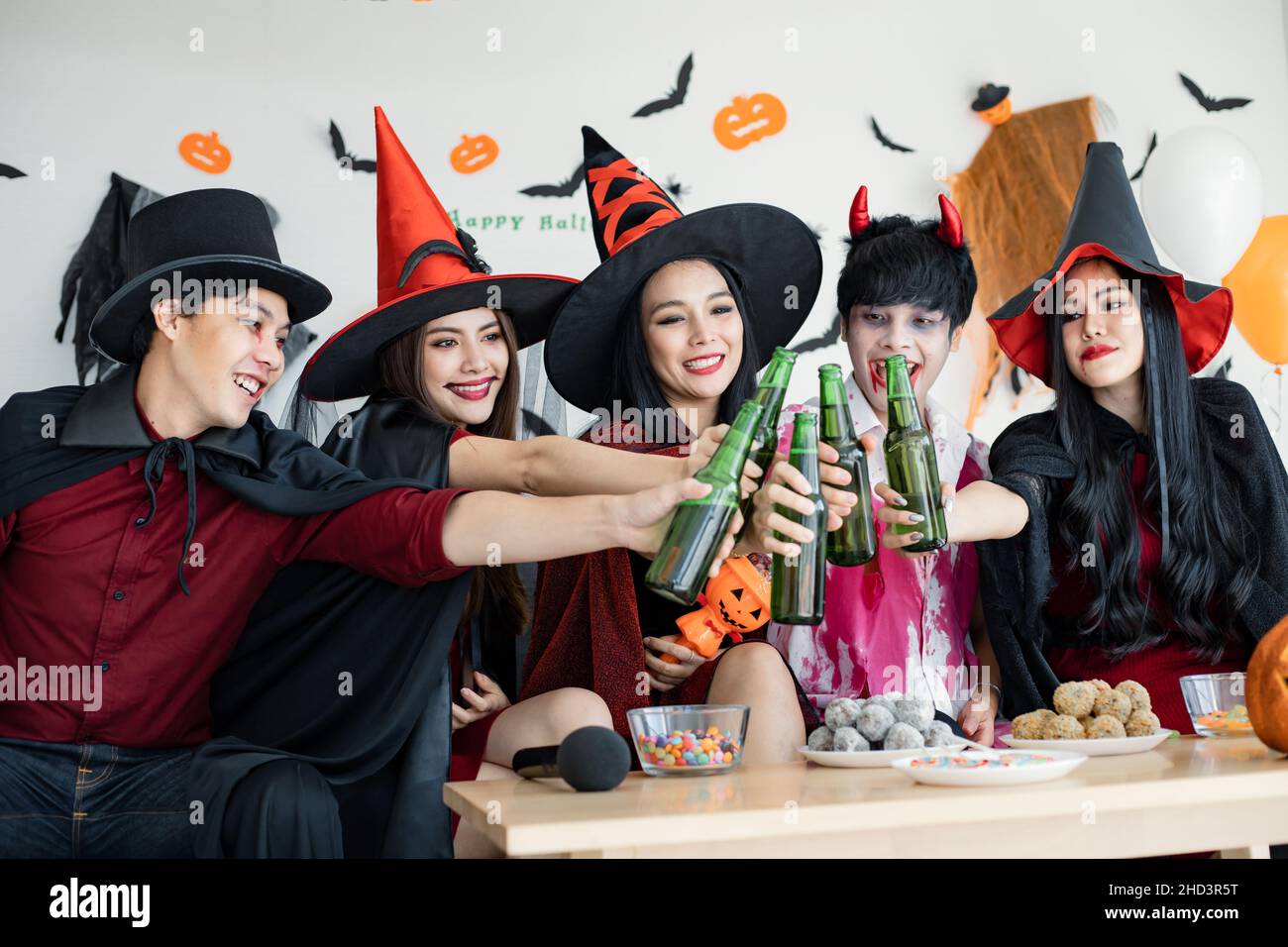 Gang of young Asian in costume witch, wizard with celebrate Halloween party for clink bottle and drink in the room. Group teen Thai with celebrate Hal Stock Photo