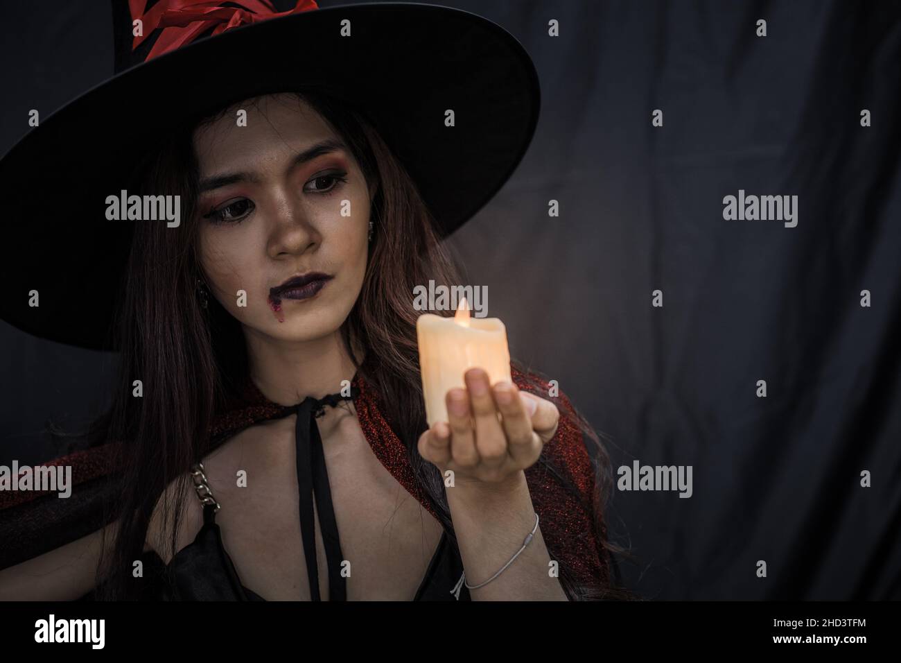 Young Asian woman in costume witch and hold candle on black cloth background of Halloween concept. Portrait of teen woman dressed up as witch for cele Stock Photo