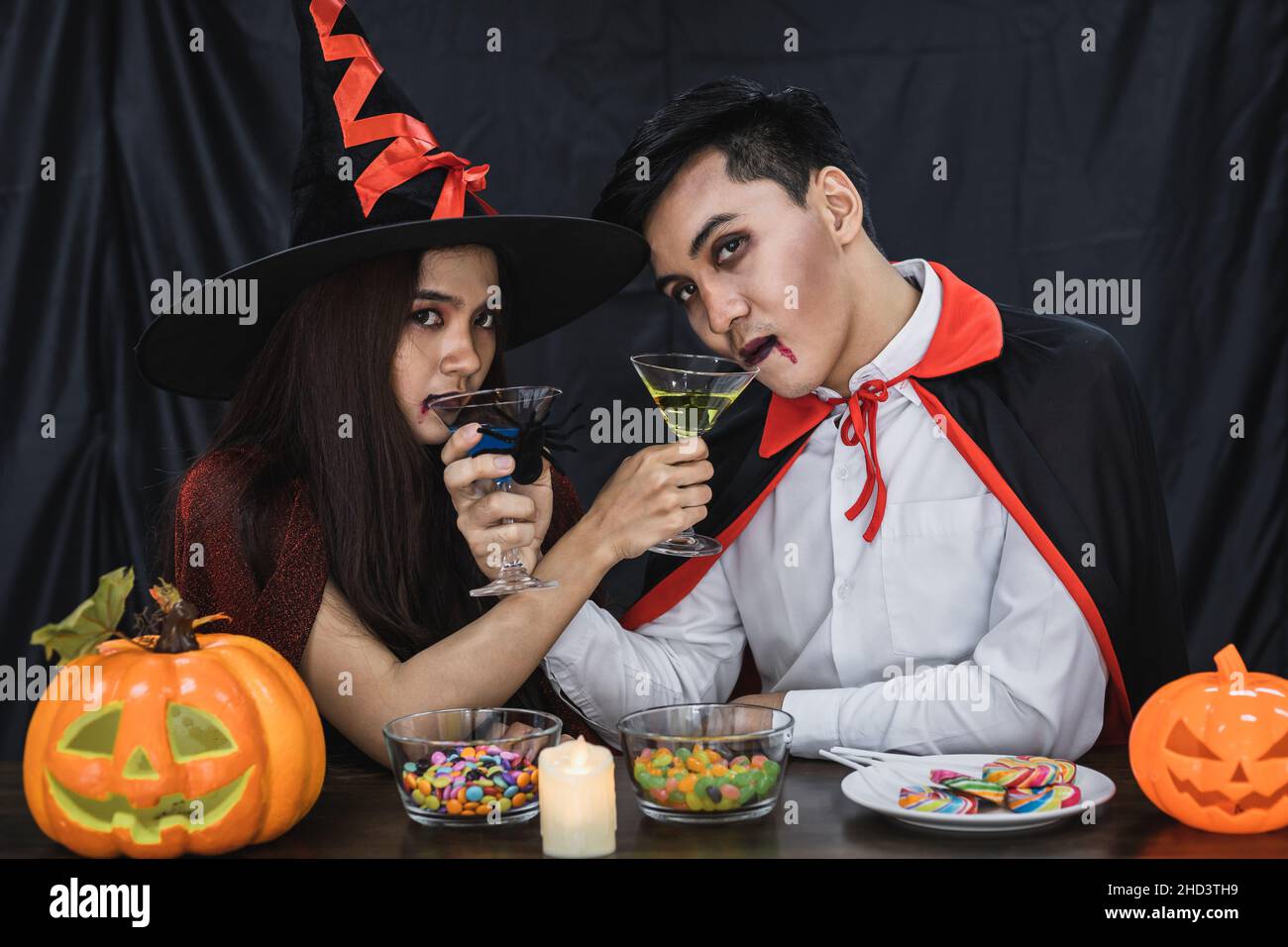 Young Asian couple in costume witch and dracula with celebrate Halloween party for clink glass and drink in Halloween festival. Couple in costume cele Stock Photo