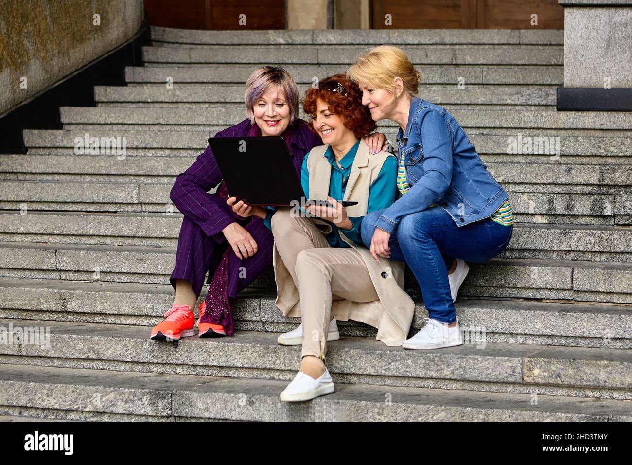Live streaming classes using laptop by three middle aged women outdoors. Stock Photo