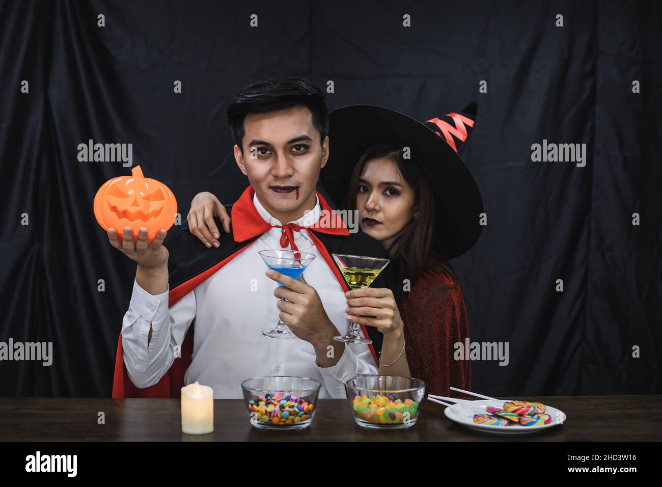 Young Asian couple in costume witch and dracula with celebrate Halloween party for clink glass and drink in Halloween festival. Couple in costume cele Stock Photo