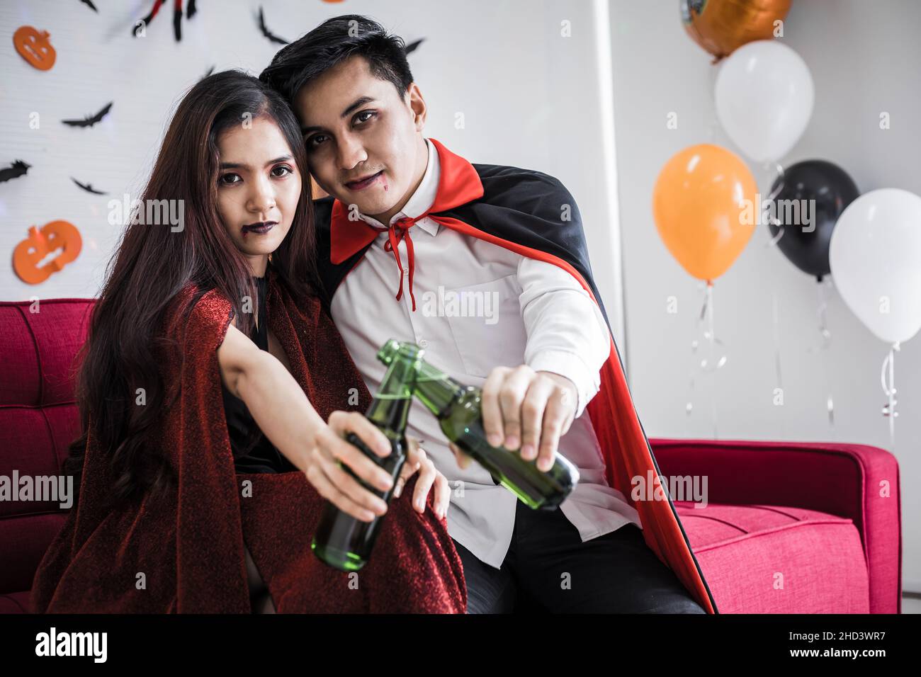 Young Asian couple in costume witch and dracula with celebrate Halloween party and drink beer together in Halloween festival  in the room at home. Con Stock Photo