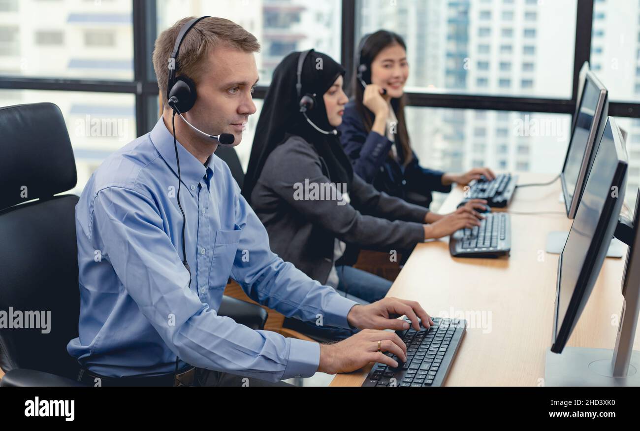 Caucasian handsome man and group of diverse telemarketing customer service staff team in call center. Call center worker accompanied by team. Smiling Stock Photo