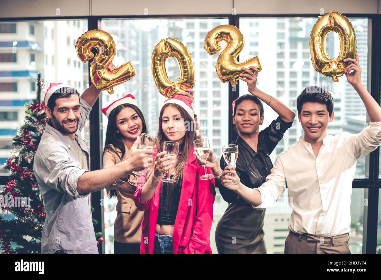 Group of office workers celebrating Christmas and New Year with clink glasses and drink prosecco, wine together while holding balloons in 2020 with ha Stock Photo