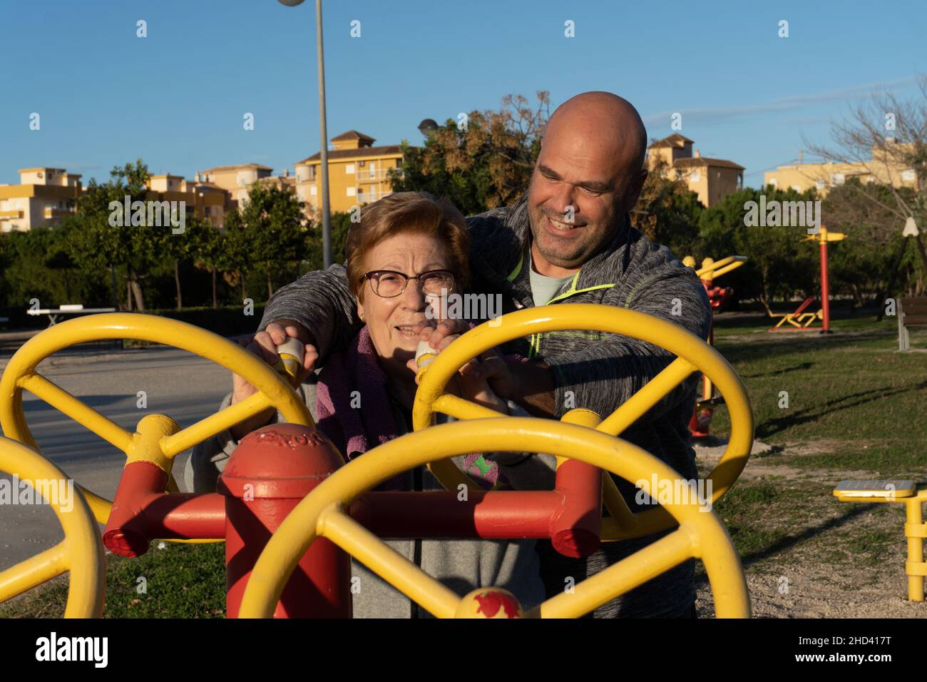 Male trainer helps older woman to exercise on the machine in a bio-healthy park Stock Photo