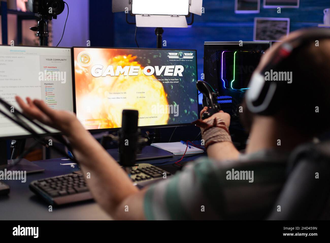 Player streaming video games with headset and losing on computer. Man looking at monitors with live stream chat and online game, playing and broadcasting gameplay with microphone. Stock Photo