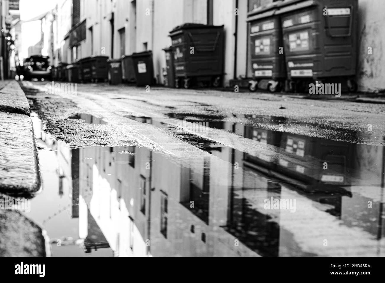 Grayscale image of a puddle on a street with a reflection of buildings and the sky Stock Photo