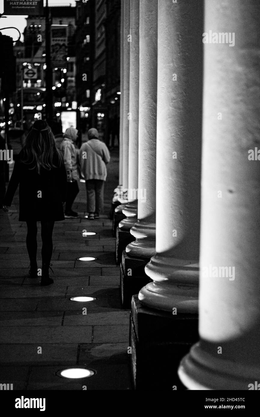 A vertical shot of people walking on a sidewalk near a hotel, London, England, grayscale image Stock Photo