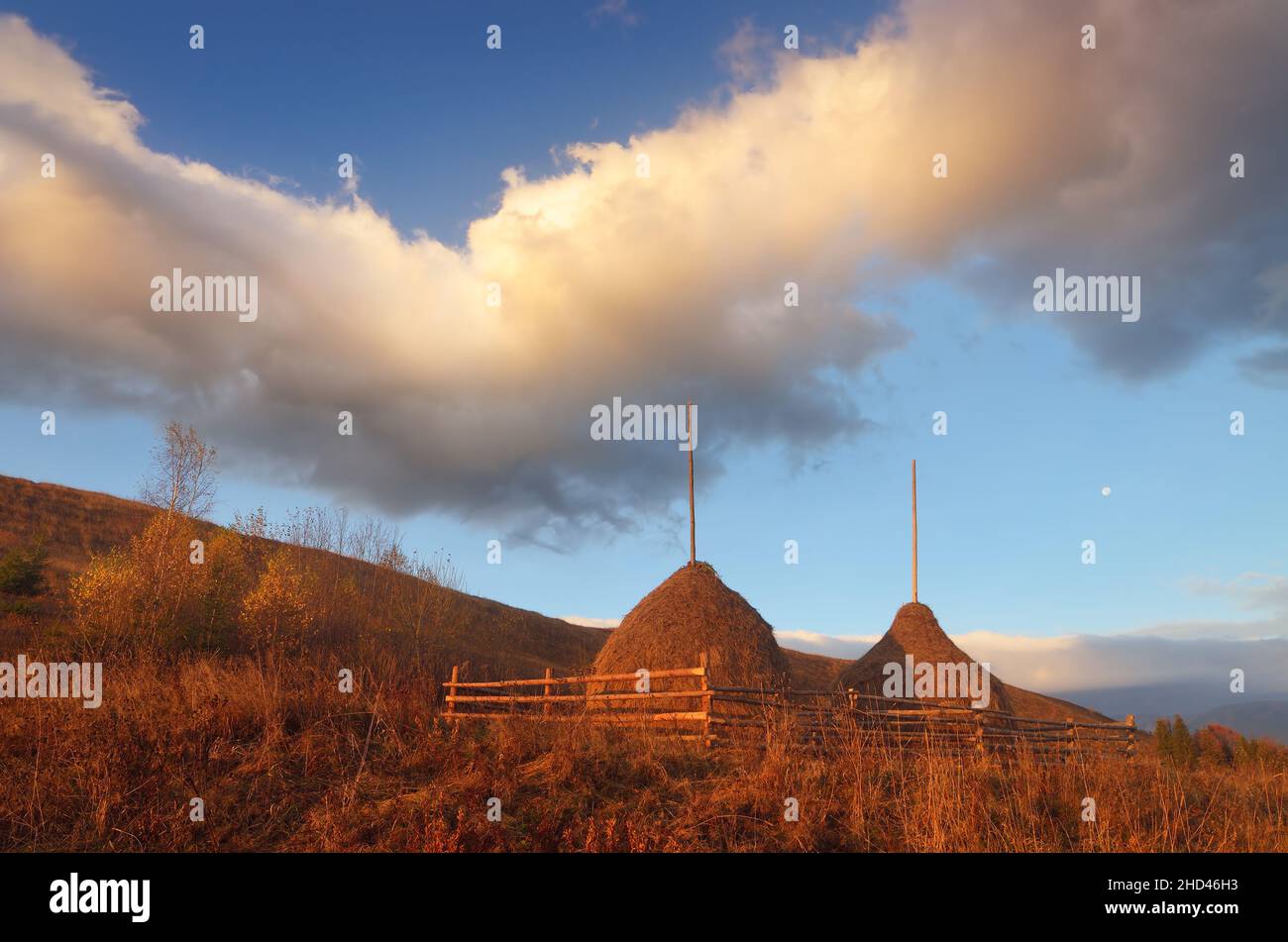 Autumn landscape in a mountain village. Two stack of dry hay. Beautiful evening clouds. Carpathian mountains, Ukraine, Europe Stock Photo