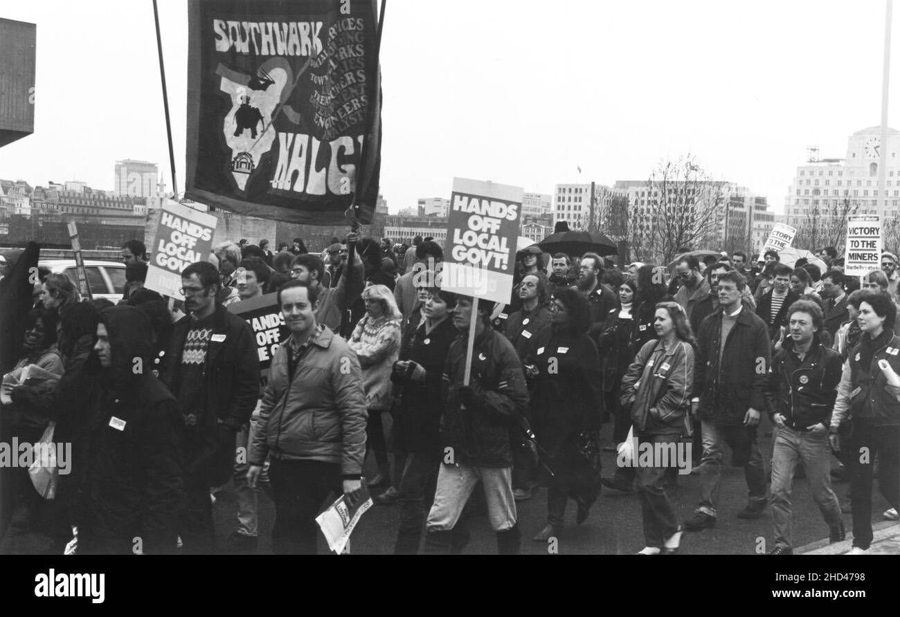A 1984 demonstration march by members of the Southwark branch of the British trade union, NALGO (National and Local Government Officers' Association) protesting against the planned abolition of the GLC (Greater London Council). The photograph depicts the marchers crossing Waterloo Bridge, London. The protestors are carrying the Southwark Branch NALGO banner, placards with the slogans, “Hands off Local Govt”, “Hands off The GLC” and also some prepared by the newspaper, ‘Socialist Worker’ showing support for the Miners’ Strike, “Victory to the Miners – Stop the Tory Attacks”. Stock Photo