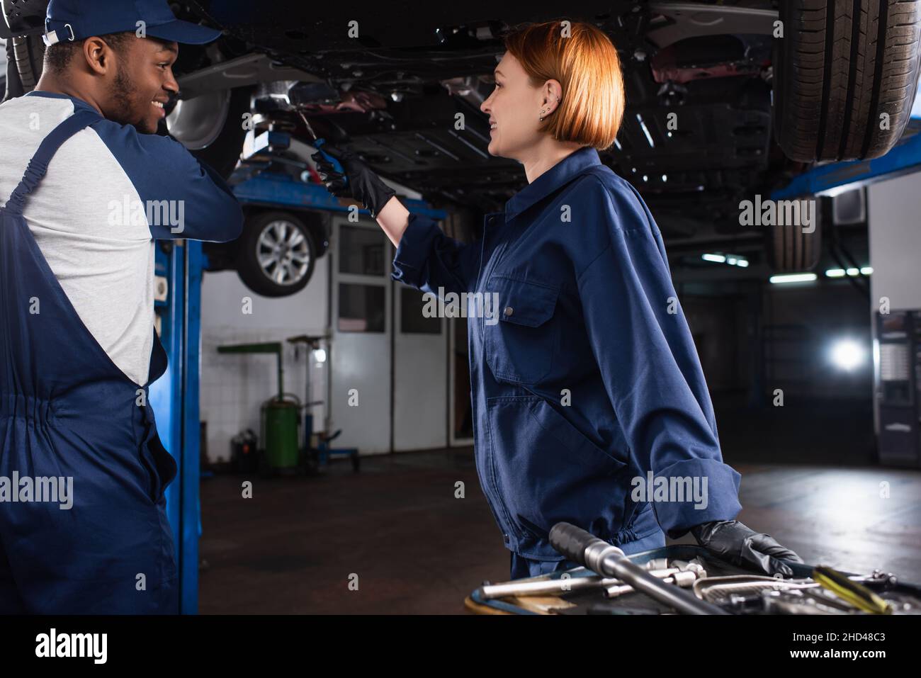 Side view of cheerful multiethnic mechanics working with car near tools