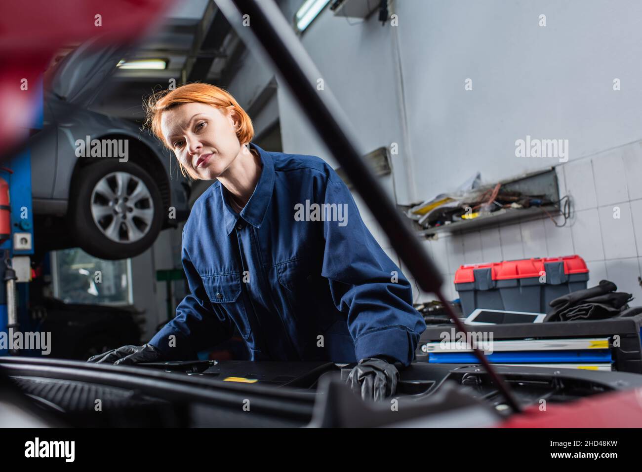 forewoman in uniform looking at camera near blurred car in workshop Stock Photo