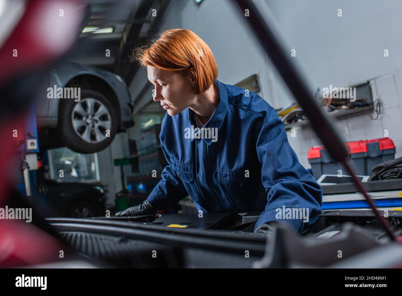 forewoman in uniform inspecting blurred car with open hood in workshop Stock Photo