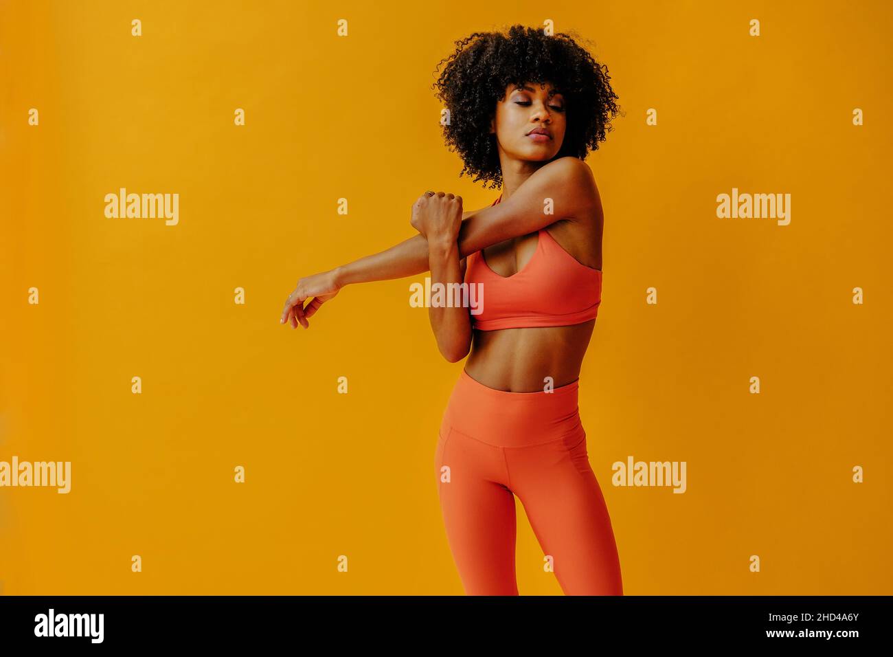 attractive young fit woman in sportswear stretching isolated on orange background Stock Photo