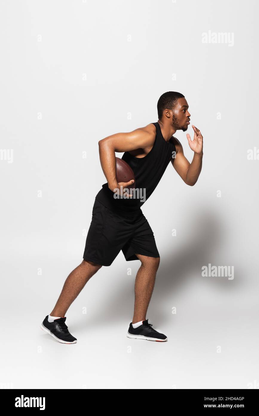 full length of african american sportsman playing rugby and running on grey Stock Photo