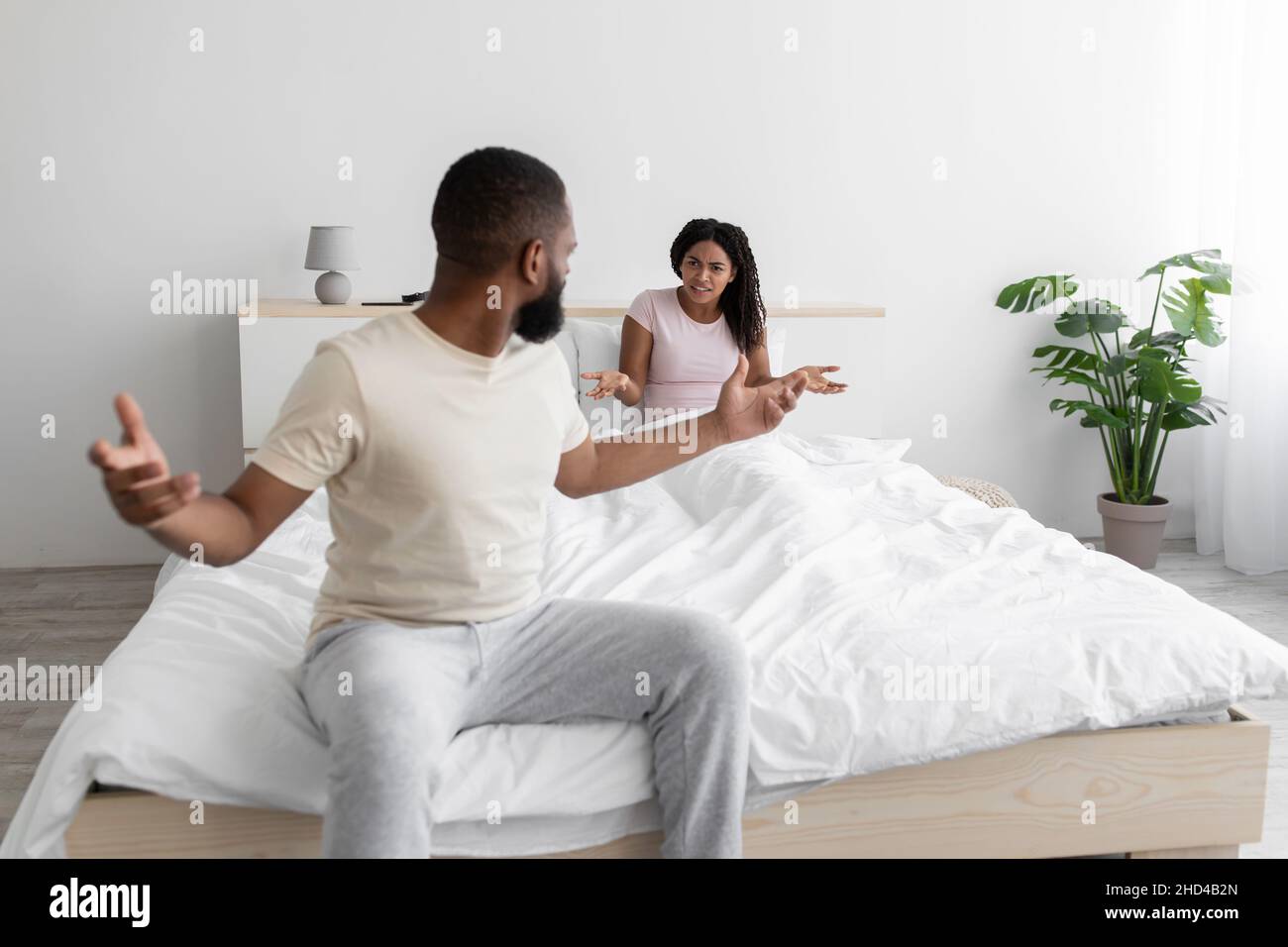 Irate unhappy excited millennial black woman and man swearing, freaking out, shouting and gesturing on bed Stock Photo