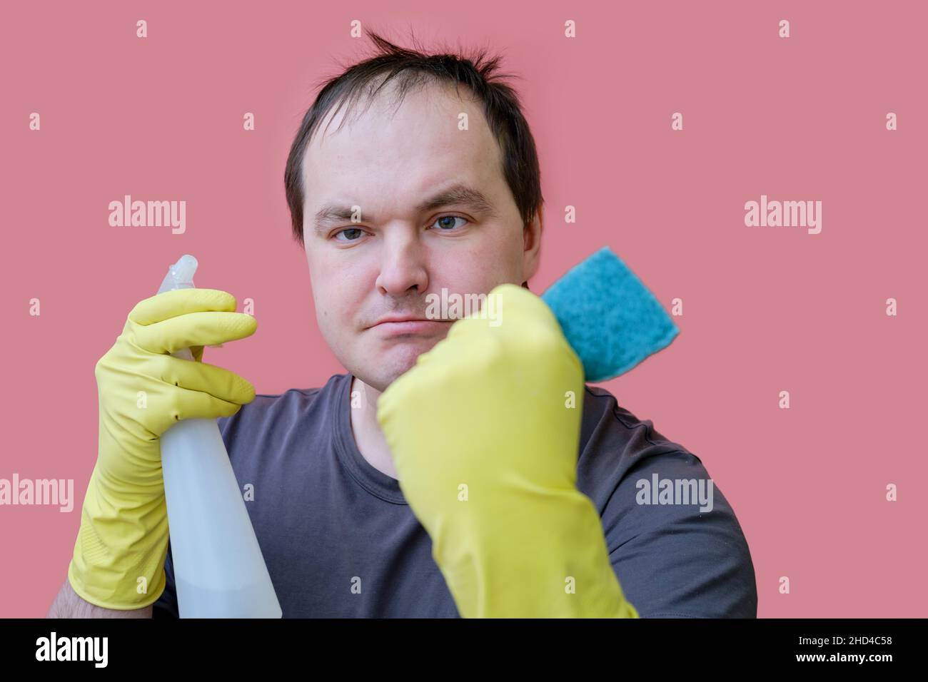 Angry male cleaner in yellow gloves, studio pink background Stock Photo