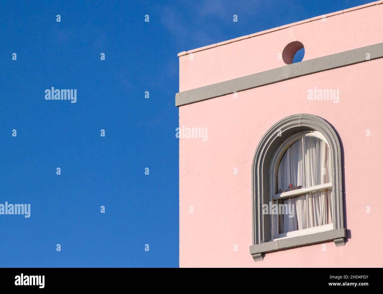 Grey Round Arch Window In A Pink Painted Building Against A Blue Sky, Christchurch UK Stock Photo