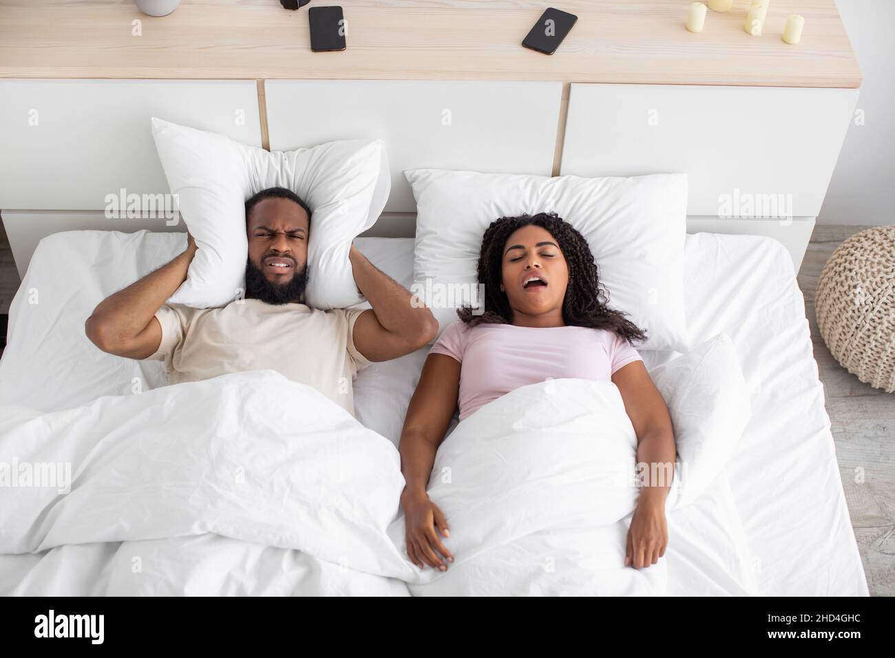 Angry disgruntled millennial black husband covers his ears with pillow
