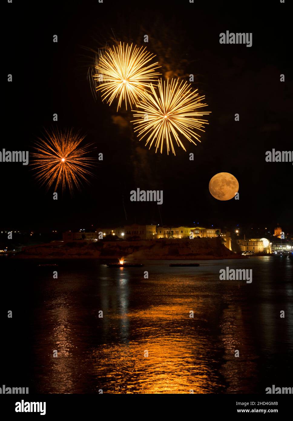 Full moon over Kalkara city in Malta with nice fireworks and its reflection in the sea during night. Night photography. Fireworks in Malta. Fireworks Stock Photo