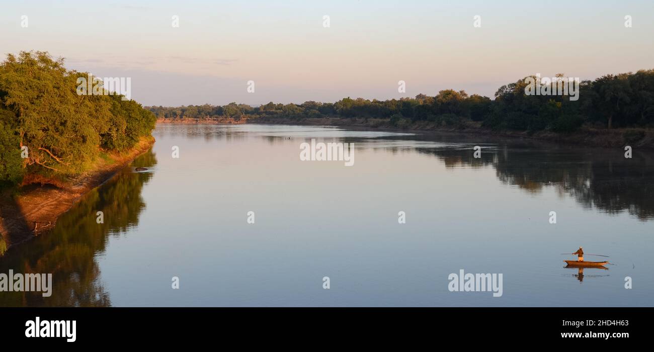 A man on a wooden boat fishing in the Luangwa river in the early morning light, South Luangwa National Park, Zambia Stock Photo
