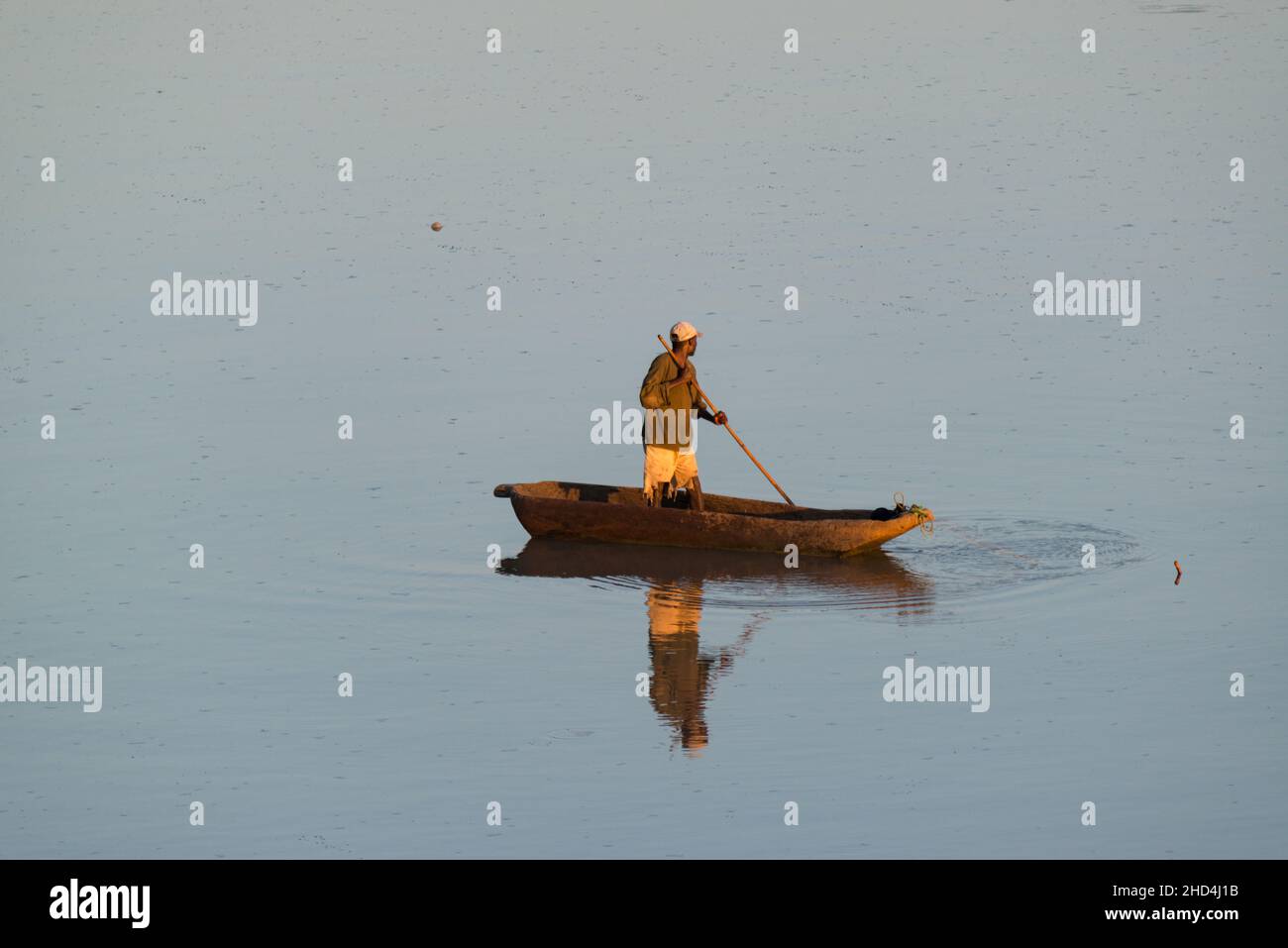 A man on a wooden boat fishing in the Luangwa river in the early morning light, South Luangwa National Park, Zambia Stock Photo