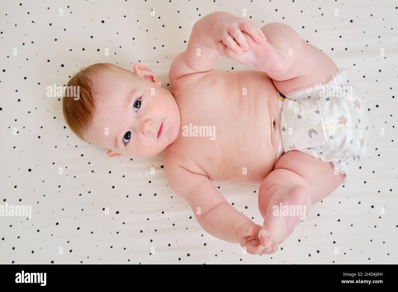 A happy infant baby with teething teeth in a diaper pulls his hand into