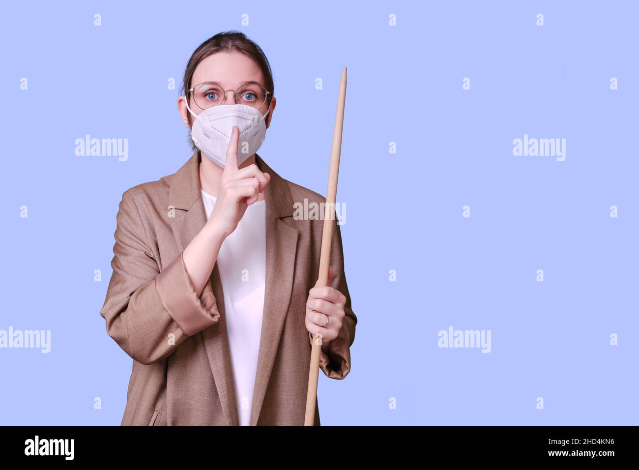 Woman teacher in medical face mask shows silence sign gesture on studio ...