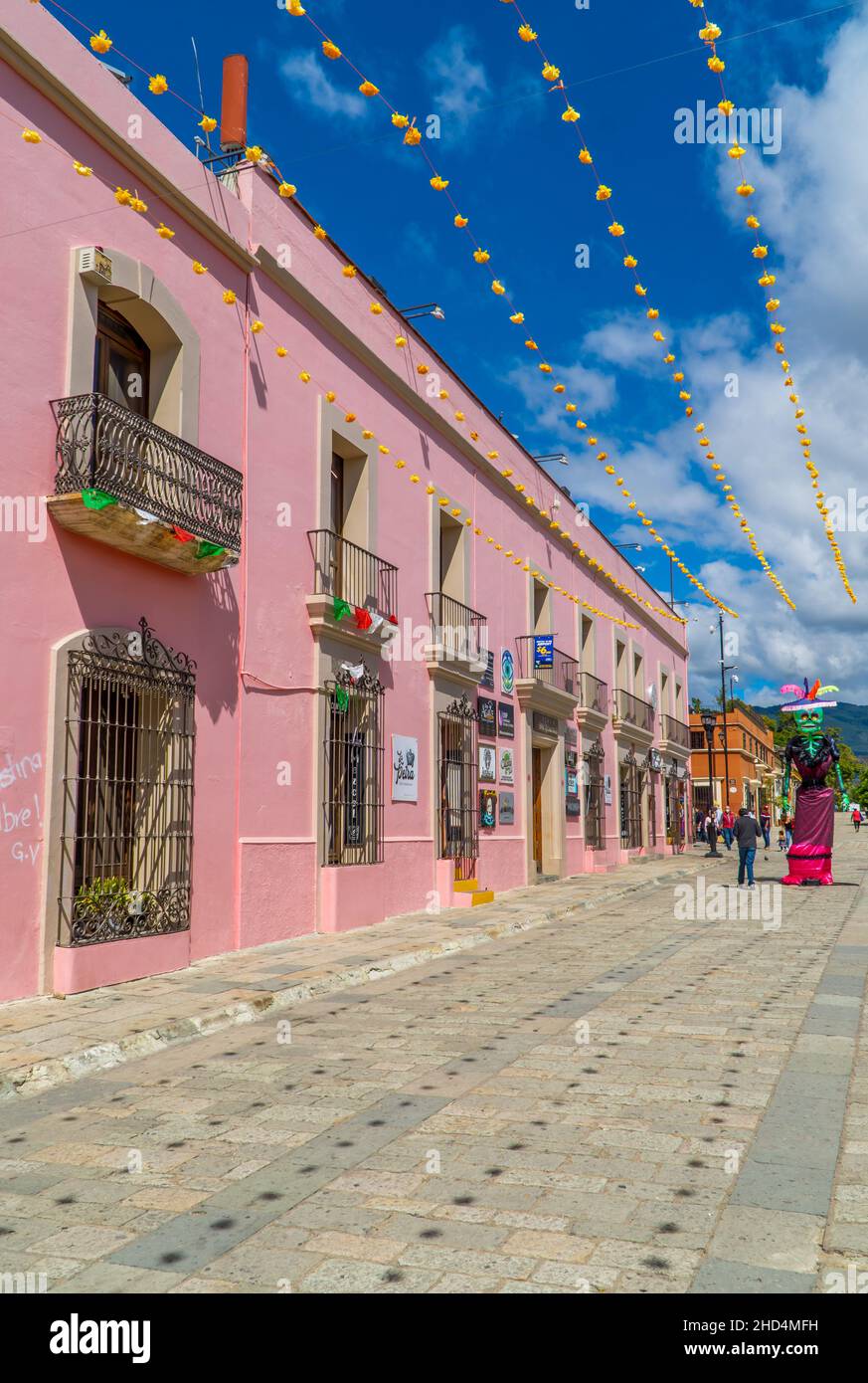 Vertical shot of people walking by colonial houses decorated for Day of the Dead in Oaxaca, Mexico Stock Photo