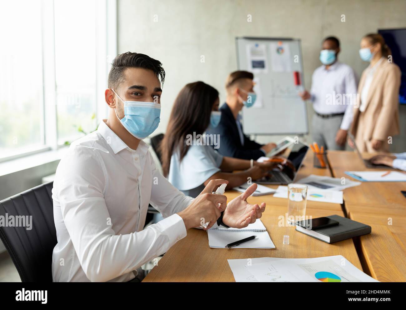Workplace Safety. Arab Businessman Wearing Medical Mask Using Disinfectant Spray In Office Stock Photo