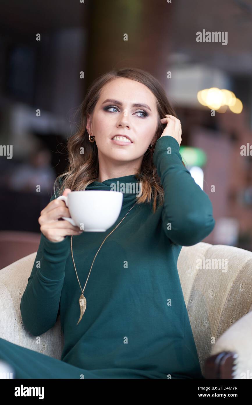A beautiful woman with a hairstyle, holding a cup of coffee, is sitting in  a cafe. He looks away with a smile straightening his hair. High quality  photo Stock Photo - Alamy