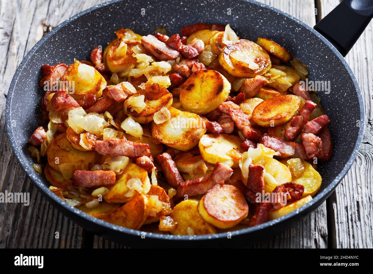 close-up of Bratkartoffeln, German fried Potatoes with Bacon and onion in a pan on a wood rustic table Stock Photo