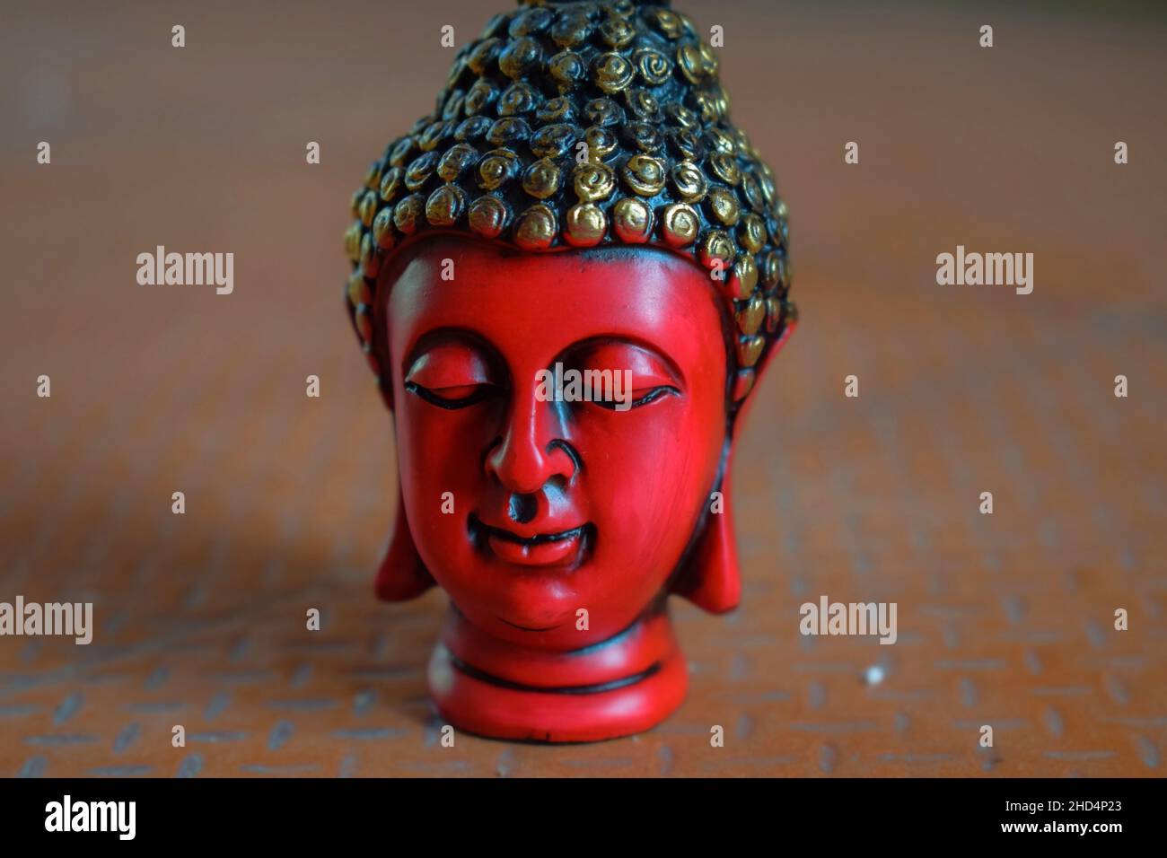 Stock photo of beautiful red color face sculpture or statue of lord buddha, head of statue painted with black and golden color on brown color backgrou Stock Photo