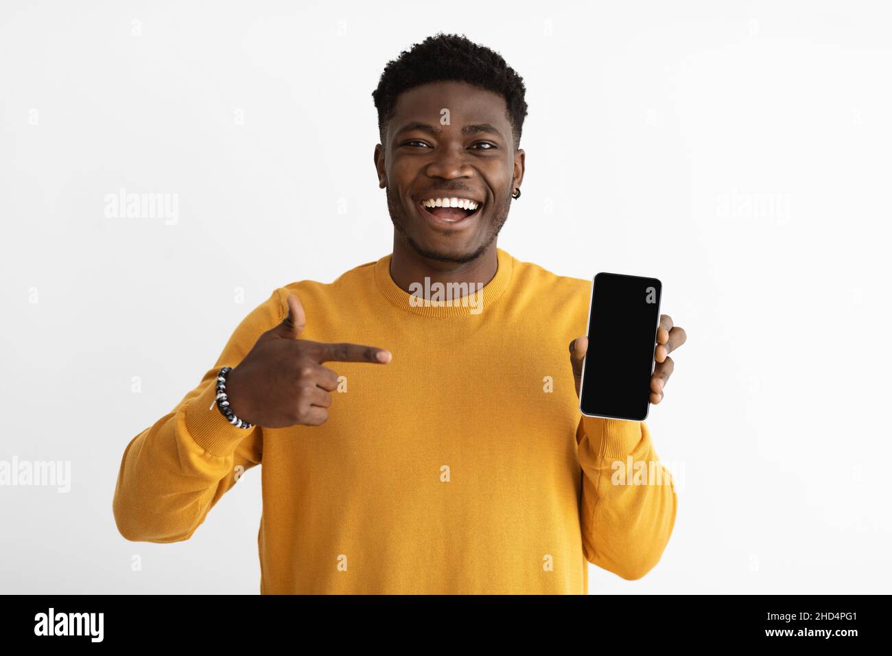 Laughing african american guy in casual pointing at smartphone, mockup Stock Photo