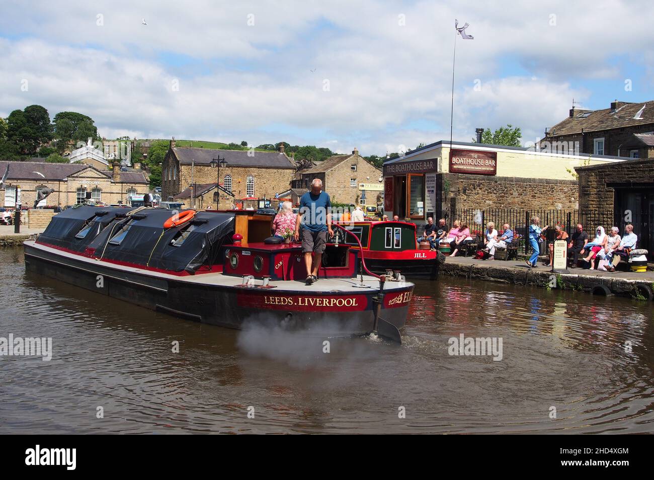 Tourists watching a passing cargo barge and enjoying the sunshine at Skipton canal basin in Yorkshire, England. Stock Photo