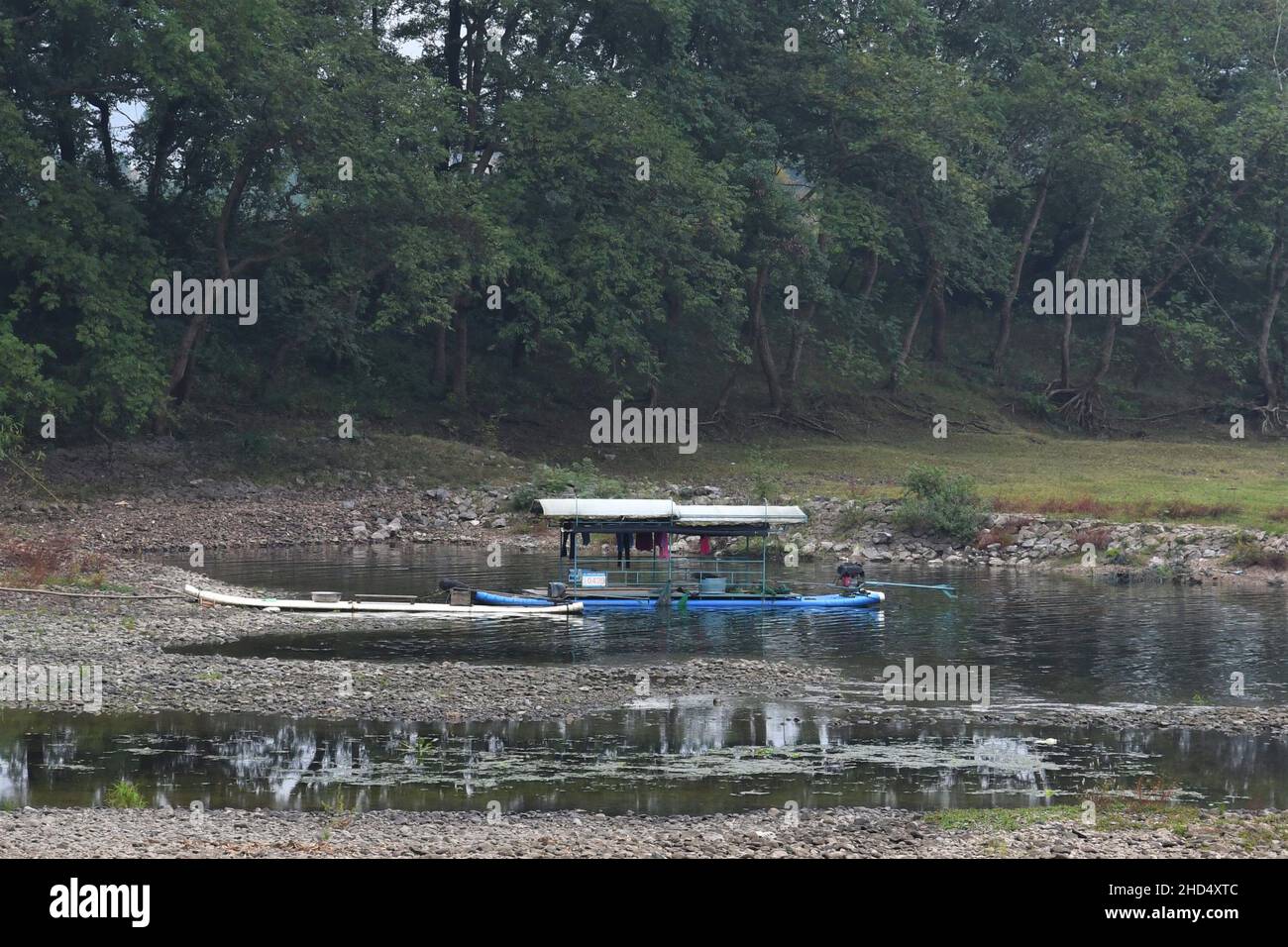 Traditional bamboo boat on Li river in Yangshuo China, with clothes drying. Green trees in the background. The boat is blue. Stock Photo