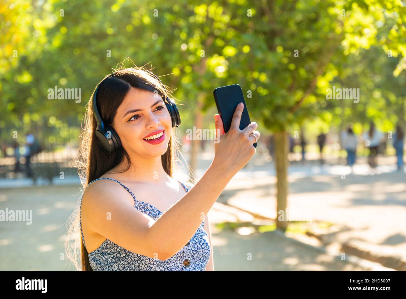 Young woman with long black hair using smart phone at park, taking a selfie. Stock Photo