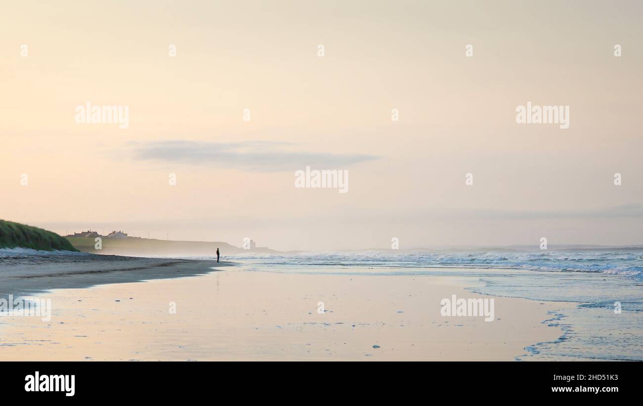 A man stands alone enjoying the peace of a quiet evening on Bamburgh beach in Northumberland. Stock Photo