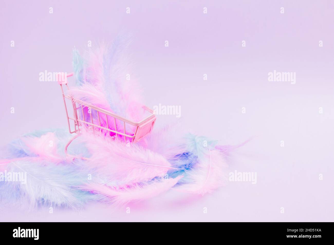 Shopping cart with soft pink and blue bird feathers inside on pink background with copy space. Minimal abstract composition. Conceptual realism. Sale Stock Photo