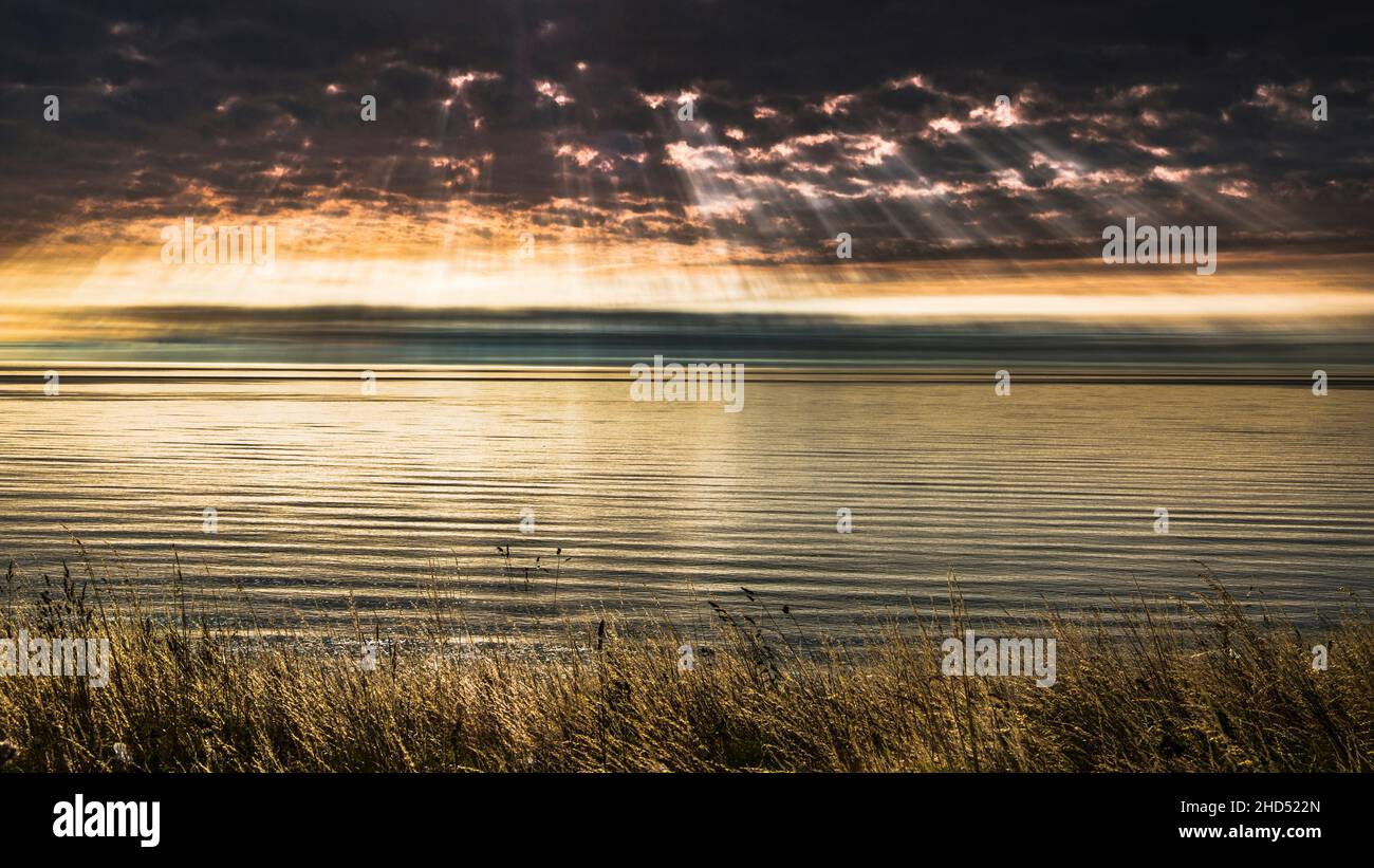 The suns rays forming through clouds over a tranquil North Sea. Stock Photo