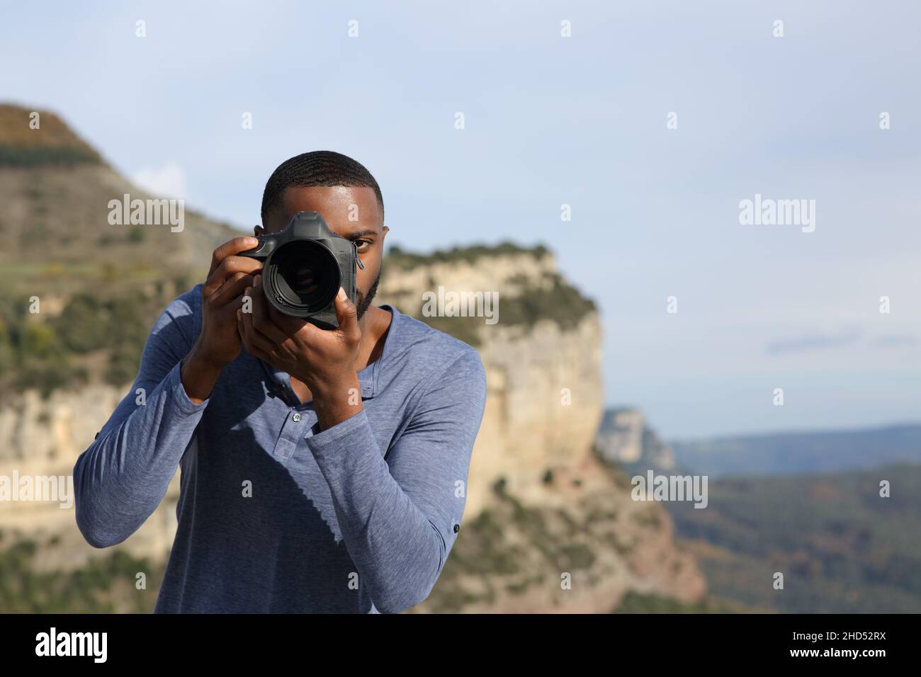 Front view portrait of a man with black skin taking photos with camera dslr in the mountain Stock Photo