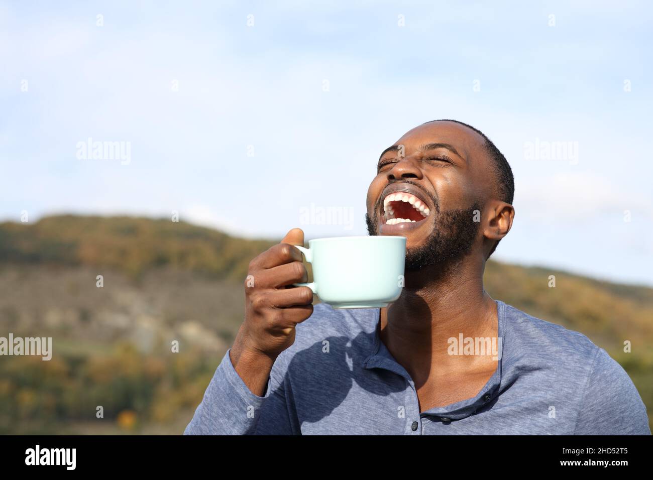 Happy man with black skin laughing and drinking coffee outdoors in the mountain Stock Photo