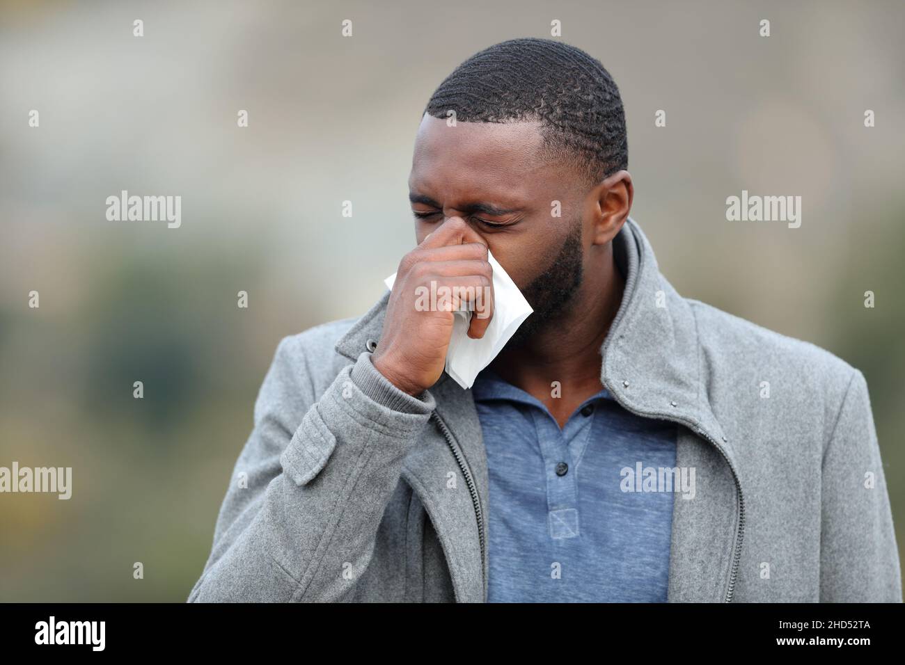 Sick guy with black skin blowing on tissue outdoors in winter Stock Photo